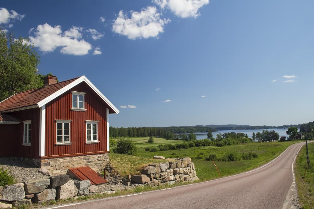 Rød hytte ved innsjø og landevei