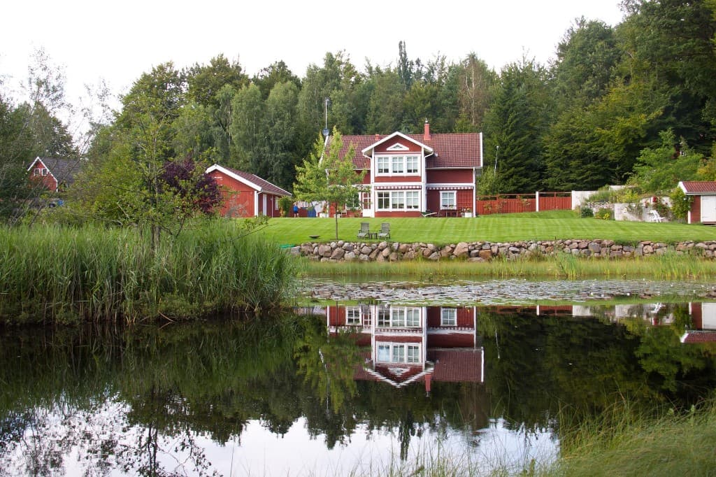 Rød svensk villa speilet i vann — privat boligsalg